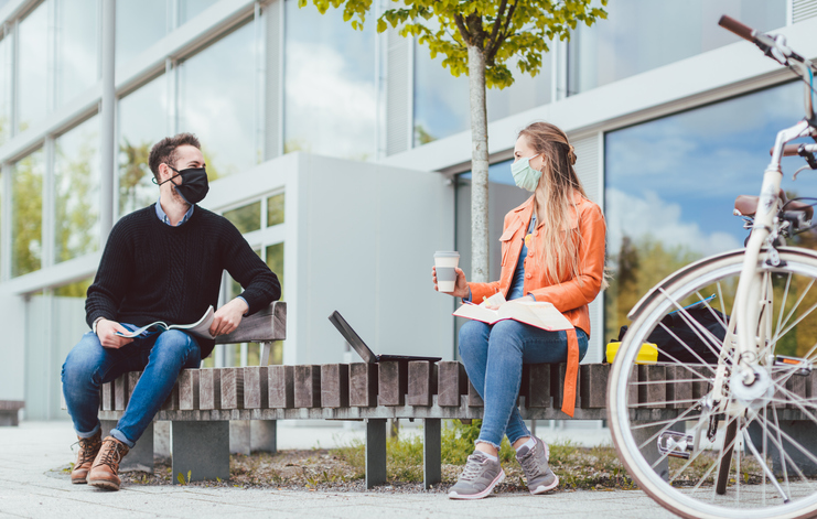 Female and male st udent in discussion while wearing face masks due to coronavirus