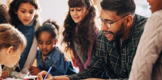 Man teaches his students how to draw in a primary school class. This elementary school educator shows his kids how to use a colouring pencil. Teaching an elementary class in a multi-ethnic school.