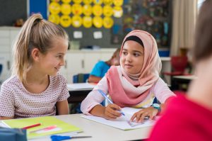 Muslim girl and Caucasian girl communicating by smiling at each other.