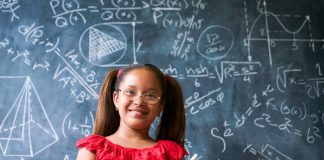 Concepts on blackboard at school. Young people, students and pupils in classroom. Smart hispanic girl writing math formula on board during lesson. Portrait of female child smiling, looking at camera